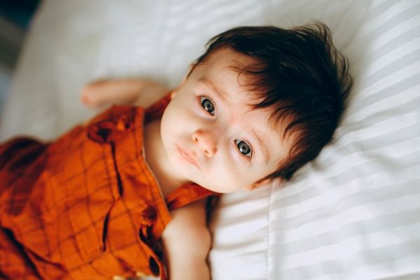 Bebé tumbado en una cama mirando a cámara Bebé niño moreno de ojos grises tumbado en una cama y mirando a cámara tiernamente