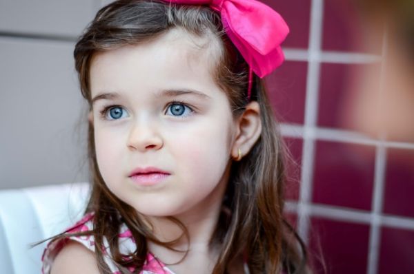 Niña morena de ojos azules brillantes y lazo fucsia en el cabello