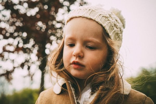 Niña con gorro de lana blanco y abrigo marrón en paisaje natural invernal