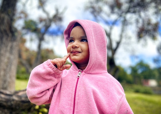 Niña con chaqueta rosa feliz en el campo Niña con chaqueta rosa y capucha puesta sonriente en un entorno natural