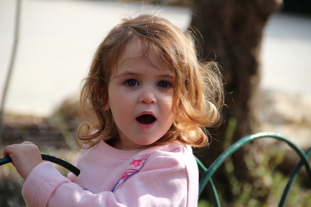 Niña sorprendida en un parque Niña en la calle mirando a cámara con expresión de sorpresa