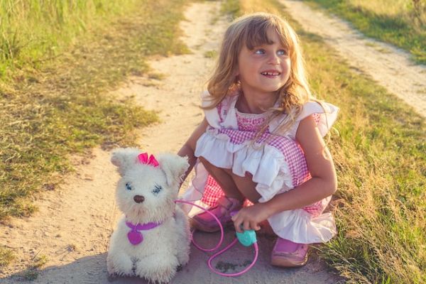 Niña rubia agachada en el campo sosteniendo la correa de su perro de peluche
