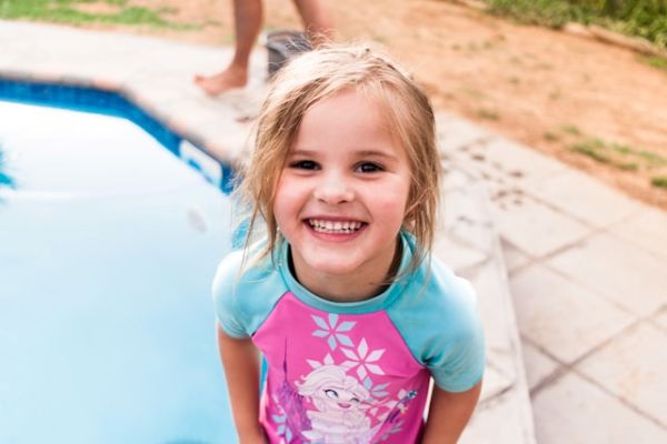 Niña rubia riendo, con traje de baño de Elsa de Frozen, junto a una piscina