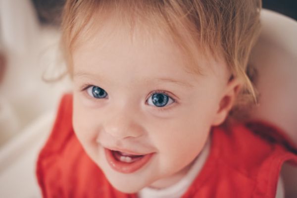 Primer plano de una niña pequeña rubia con ojos azules que sonríe mirando a la cámara