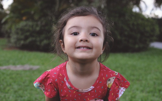 Niña en un parque mirando a cámara Niña con vestido rojo en un parque mirando a cámara