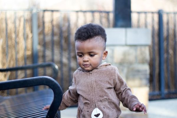 Niño con chaqueta marrón mirando hacia abajo Niño con chaqueta marrón tocando un banco con la mano y mirando hacia el suelo