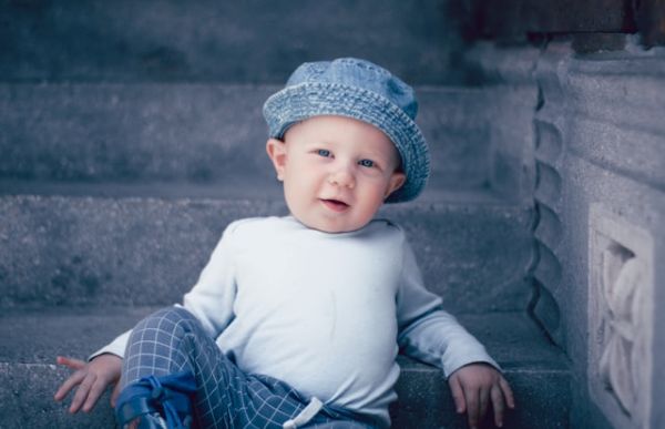 Niño sentado en unas escaleras mirando a cámara Niño con gorro tejano sentado en unas escaleras mirando a cámara