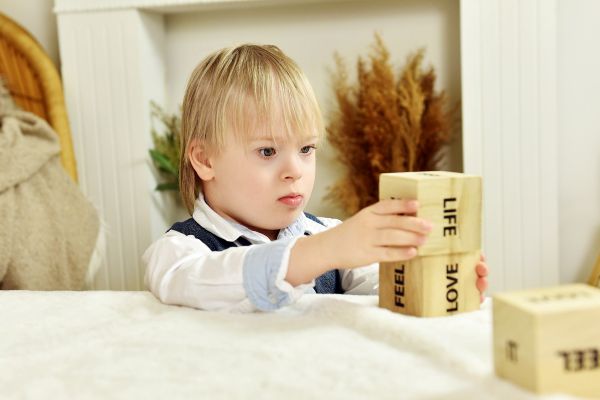 Niño rubio construyendo una torre con cubos de madera que contienen las palabras "life" y "love"