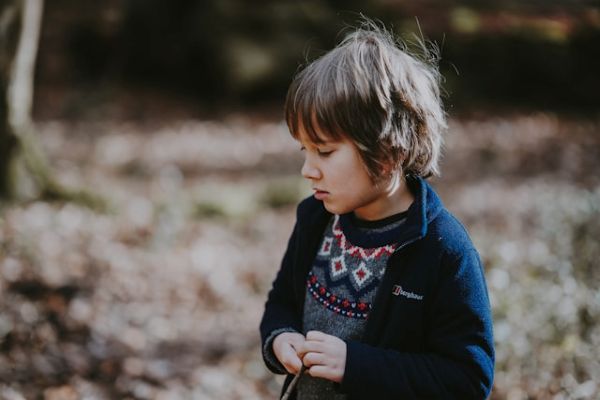 Niño con melena morena mirando hacia abajo en un paisaje otoñal 