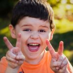 Niño feliz sonriendo a la cámara y haciendo el signo de victoria con las manos