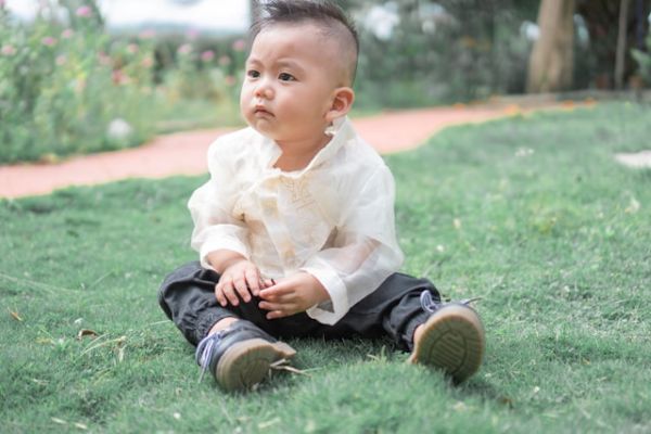 Niño asiático sentado en el césped Niño asiático sentado en el césped y cogiendo unas ramas con las manos