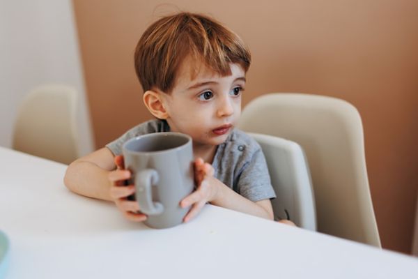 Niño sentado en una silla sosteniendo una taza que apoya en una mesa