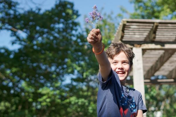 Niño sonriente levantando con la mano un pequeño ramo de flores lilas