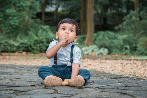Niño moreno jugando con piedras sentado en el suelo en un parque 