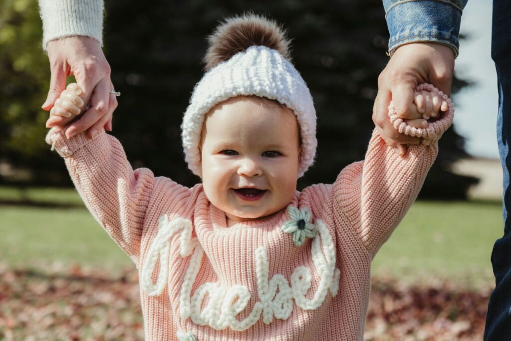 Bebé sonriente andando cogiendo la manos de sus padres
