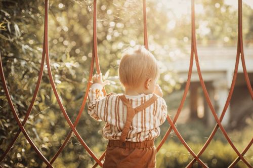 Bebé de espaldas agarrando unas rejas 