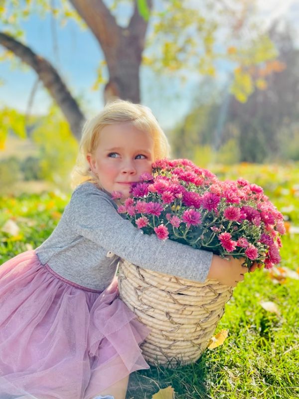 Niña sentada en el campo sosteniendo una planta con flores rosas