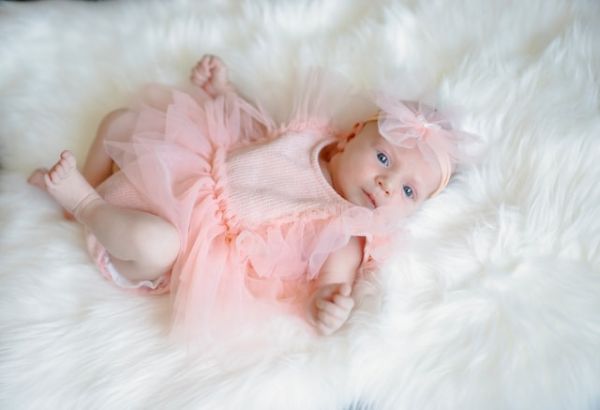 Bebé niña con vestido y lazo en la cabeza rosa acostada en una manta de pelo blanca