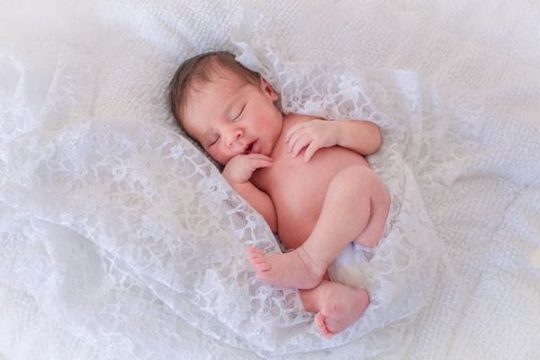 Bebé niña durmiendo acurrucada entre sábanas blancas