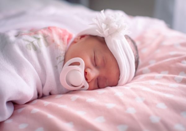 Bebé recién nacida con chupete y diadema rosa durmiendo